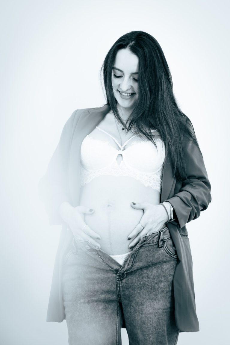 Schwangere Frau in modischer Kleidung, die liebevoll ihren Bauch hält.