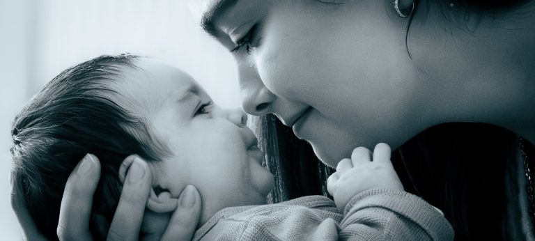 Eine Mutter lächelt liebevoll ihr Baby an, beide lächeln sich an.