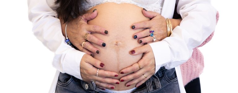 Hände legen sich liebevoll um einen sichtbar schwangerem Bauch.