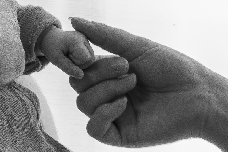 Eine kleine Hand greift sanft nach einem Fingern einer größeren Hand.