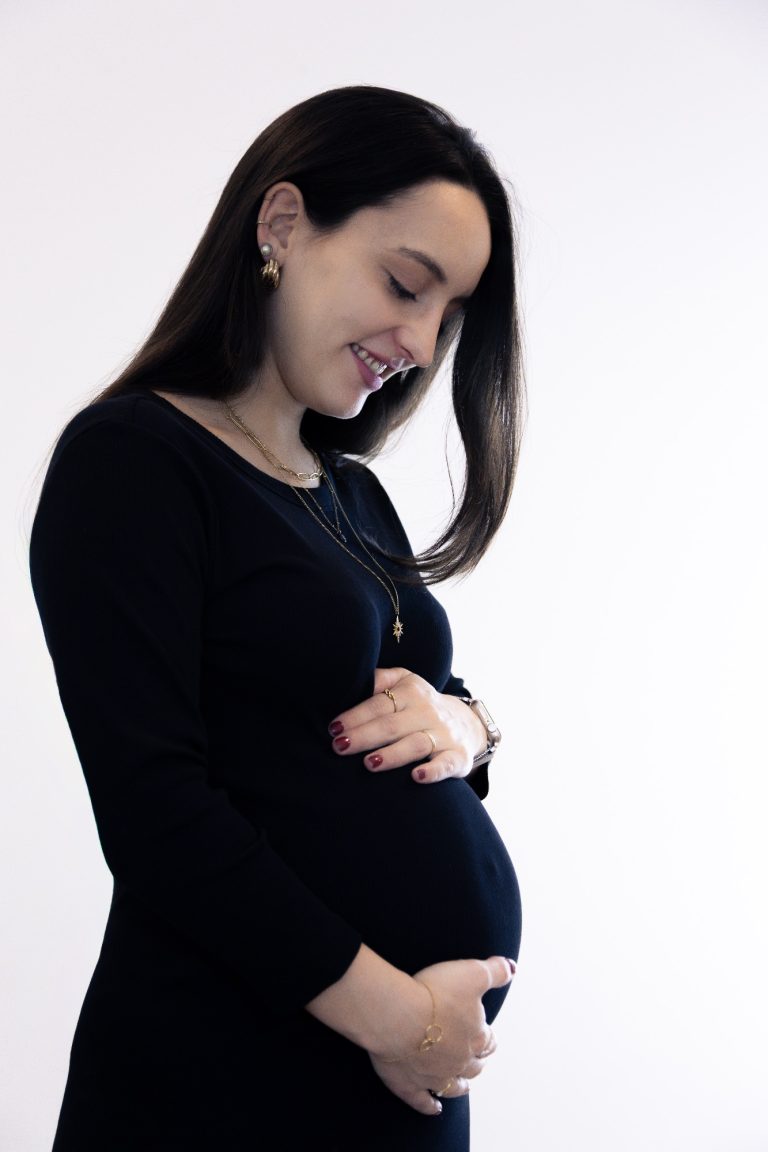 Schwangere Frau in Schwarz, lächelt und hält ihren Bauch.