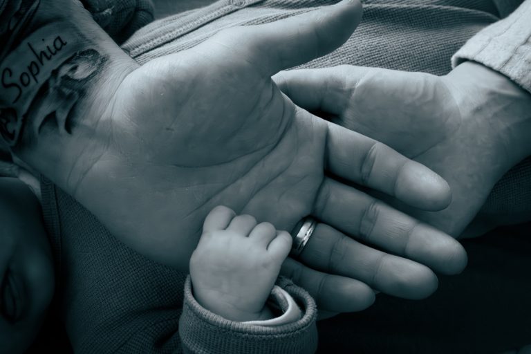 Eine kleine Hand liegt in einer größeren Hand, die einen Ring trägt.