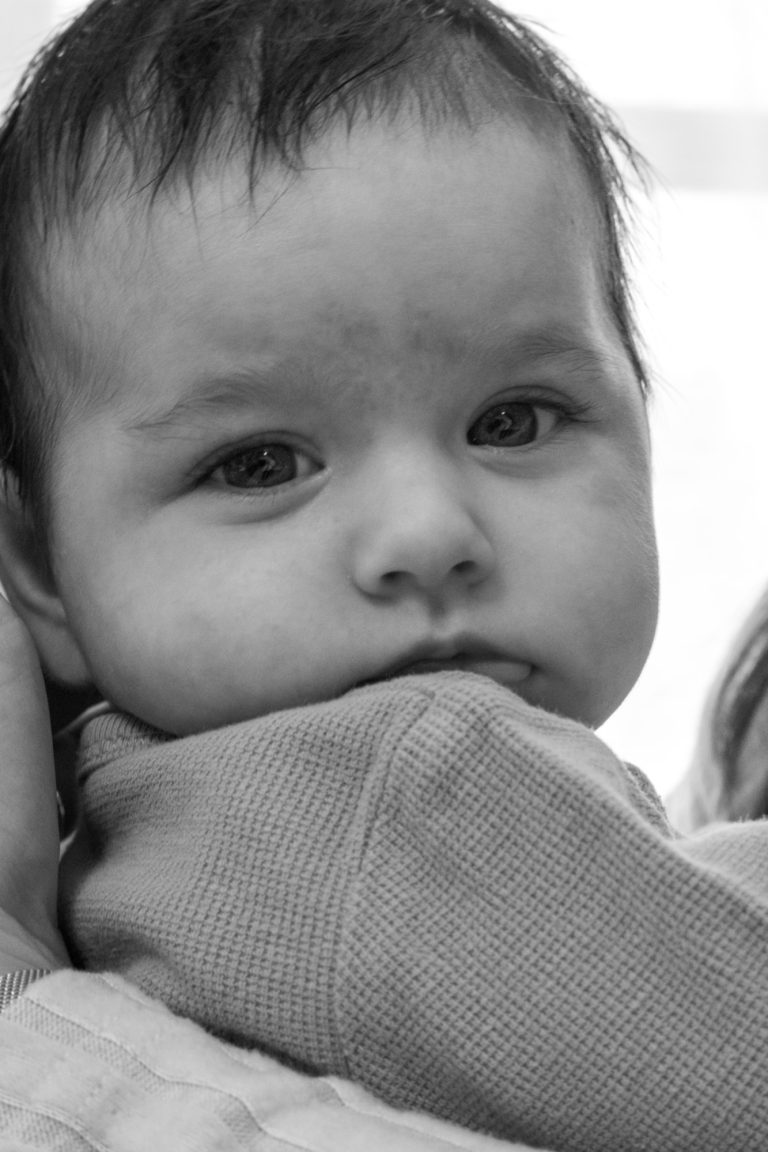 Ein kleines Kind mit ernstem Gesichtsausdruck, das in den Armen einer Person gehalten wird.