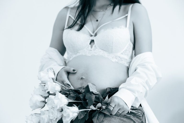 Schwangere Frau in Unterwäsche mit Blumen, sanfte Schwarz-Weiß-Darstellung.