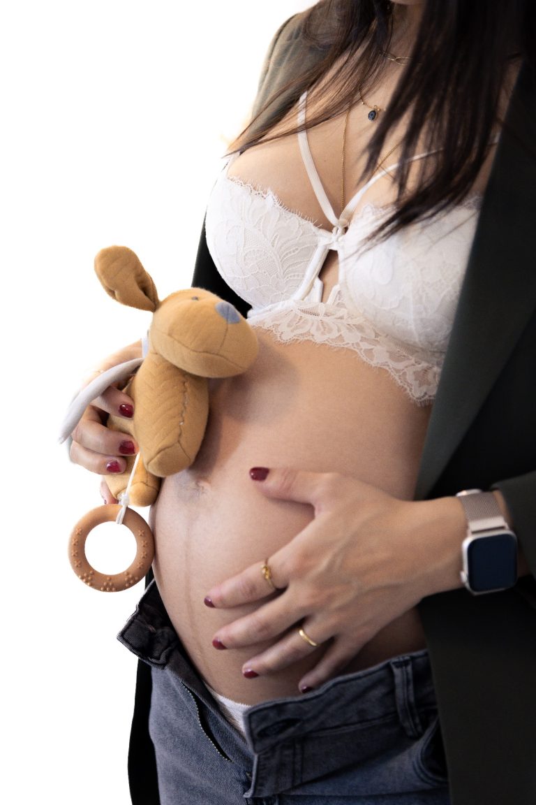 Schwangere Frau hält ein Stofftier an ihrem Bauch.