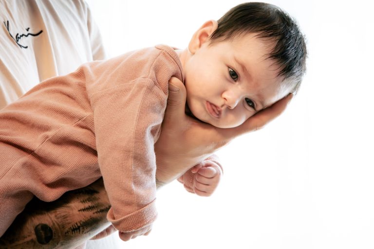 Ein Erwachsener hält ein Baby in einer sanften Position. Das Baby blickt nachdenklich.