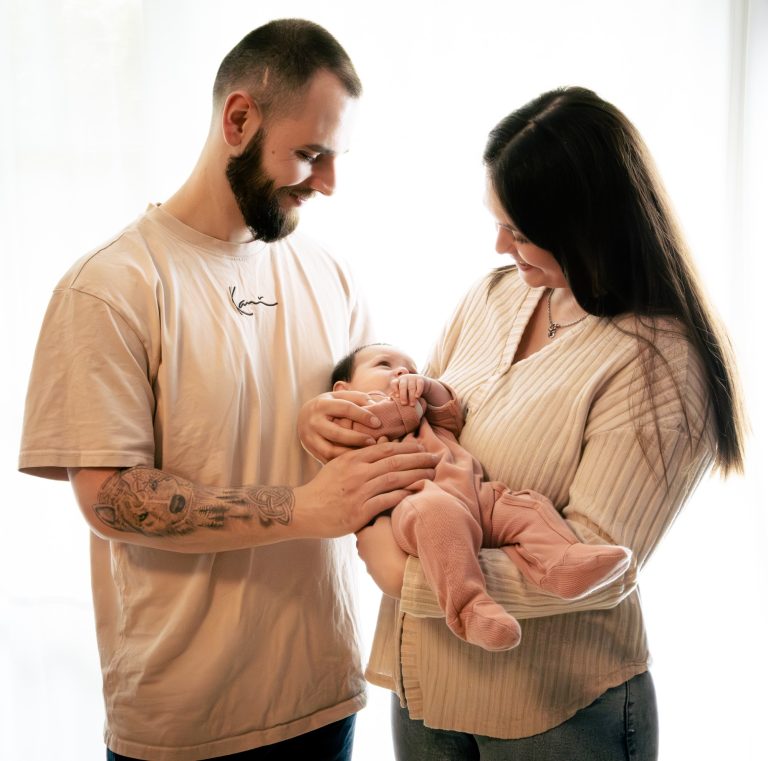 Ein Elternpaar hält ein Neugeborenes im Arm, umgeben von sanftem Licht.
