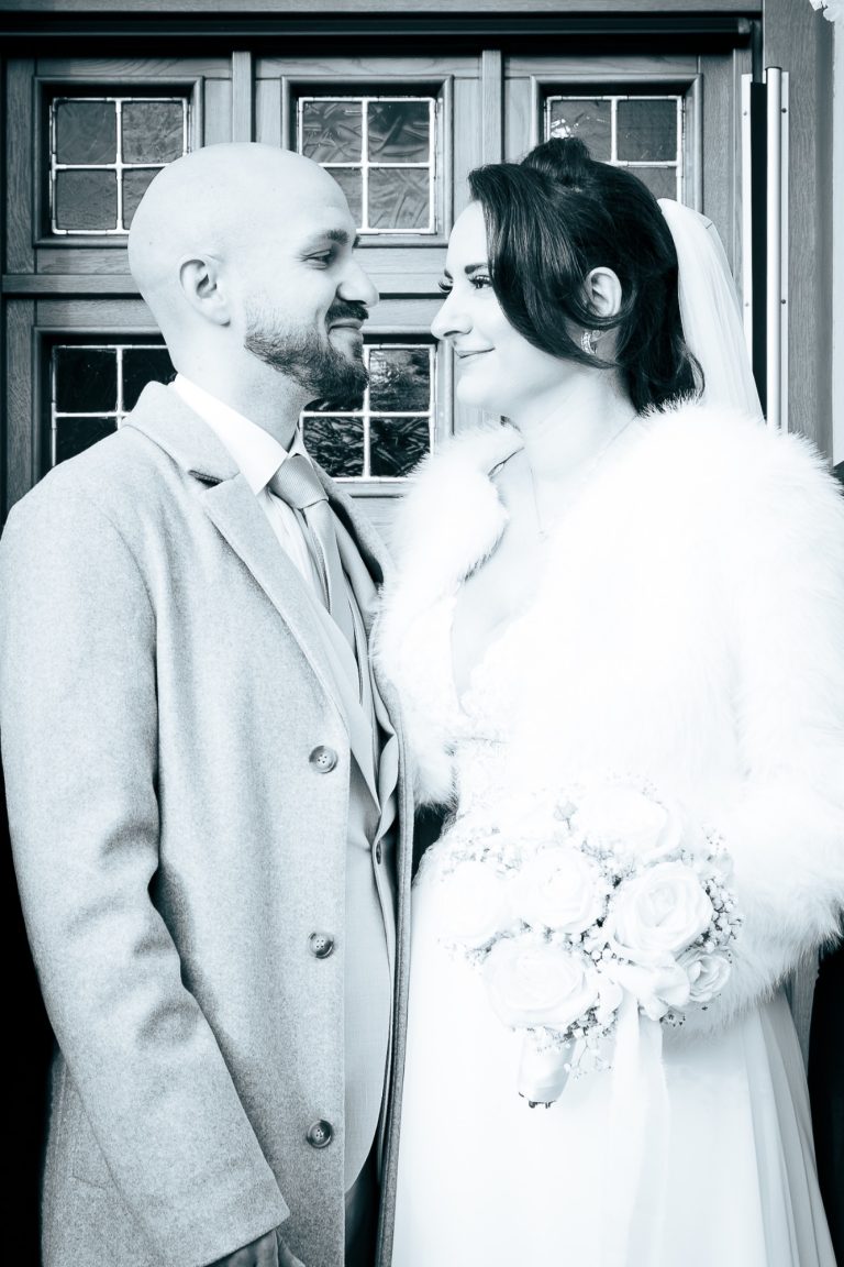 Ein Brautpaar steht sich gegenüber, lächelt sich an und trägt elegante Hochzeitskleidung.