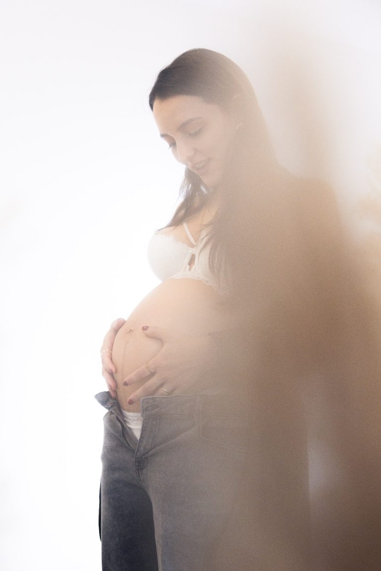 Schwangere Frau hält ihren Bauch mit einem sanften Lächeln.