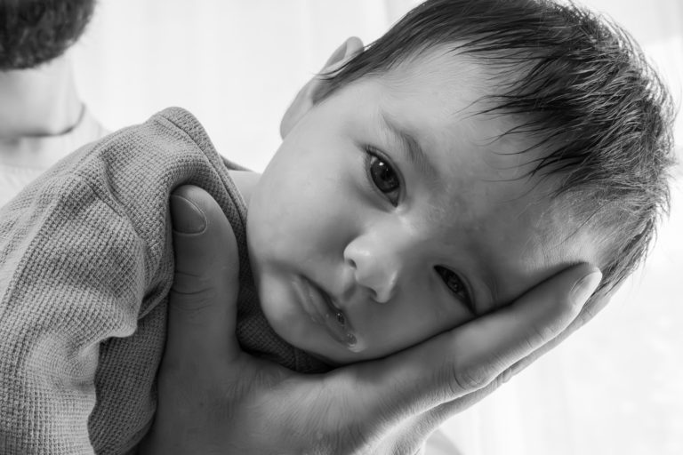 Ein Baby wird sanft von einer Hand gehalten, mit einem nachdenklichen Gesichtsausdruck.