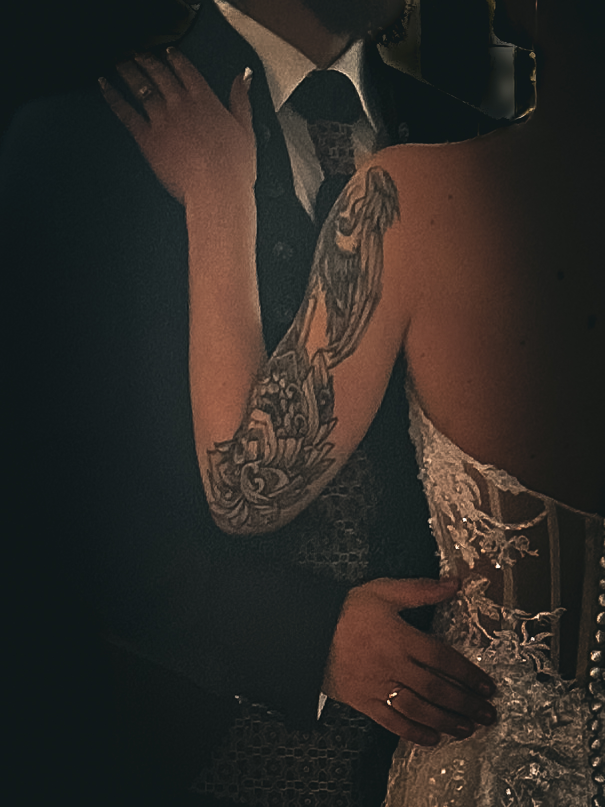 Hochzeitskleid und tätowierte Arm eines Paares, naher Blick auf ihre Umarmung.