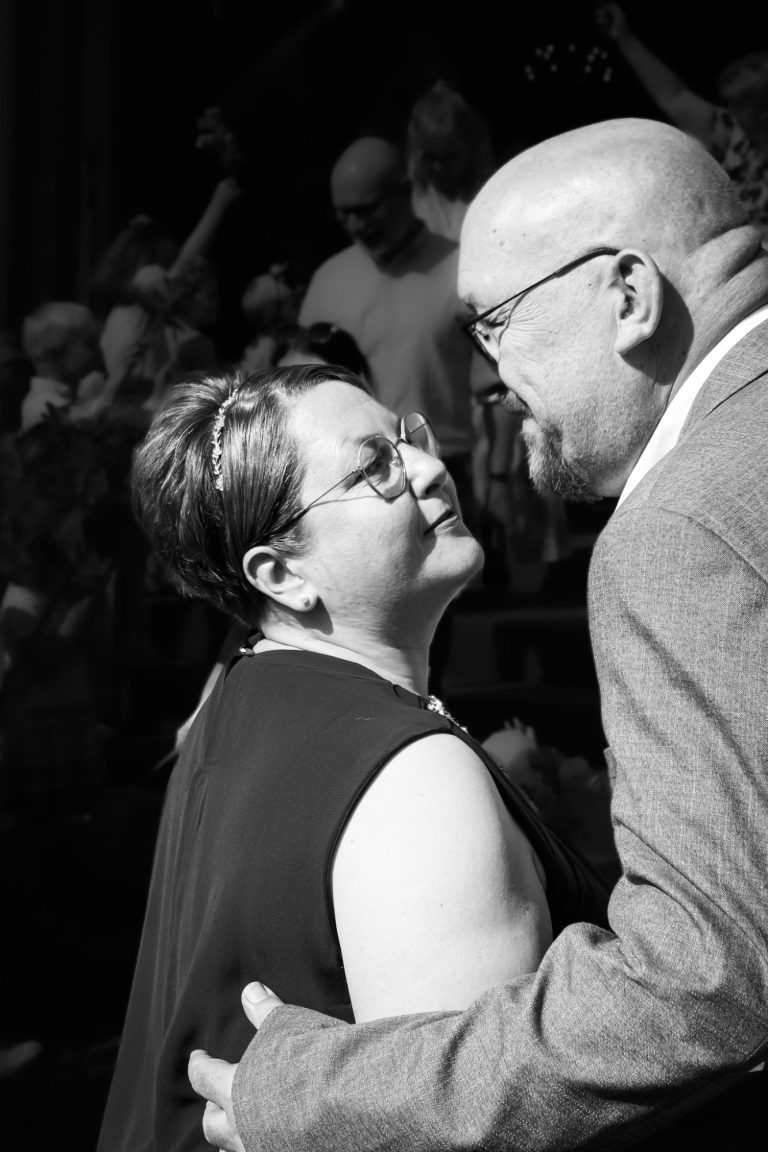 Ein Paar umarmt sich verliebt, lächelt und steht in einer festlichen Umgebung.