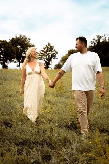 Ein Paar läuft Hand in Hand durch eine Wiese unter einem bewölkten Himmel.