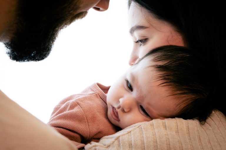 Ein Elternteil hält ein Baby sanft im Arm, beide schauen liebevoll zueinander.
