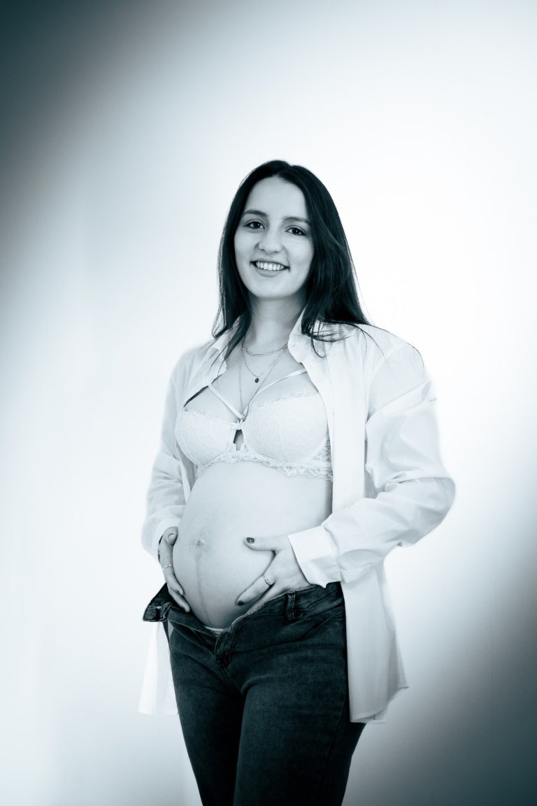 Schwangere Frau mit leichtem Lächeln, die ihren Bauch hält, in monochromatischer Farbgebung.