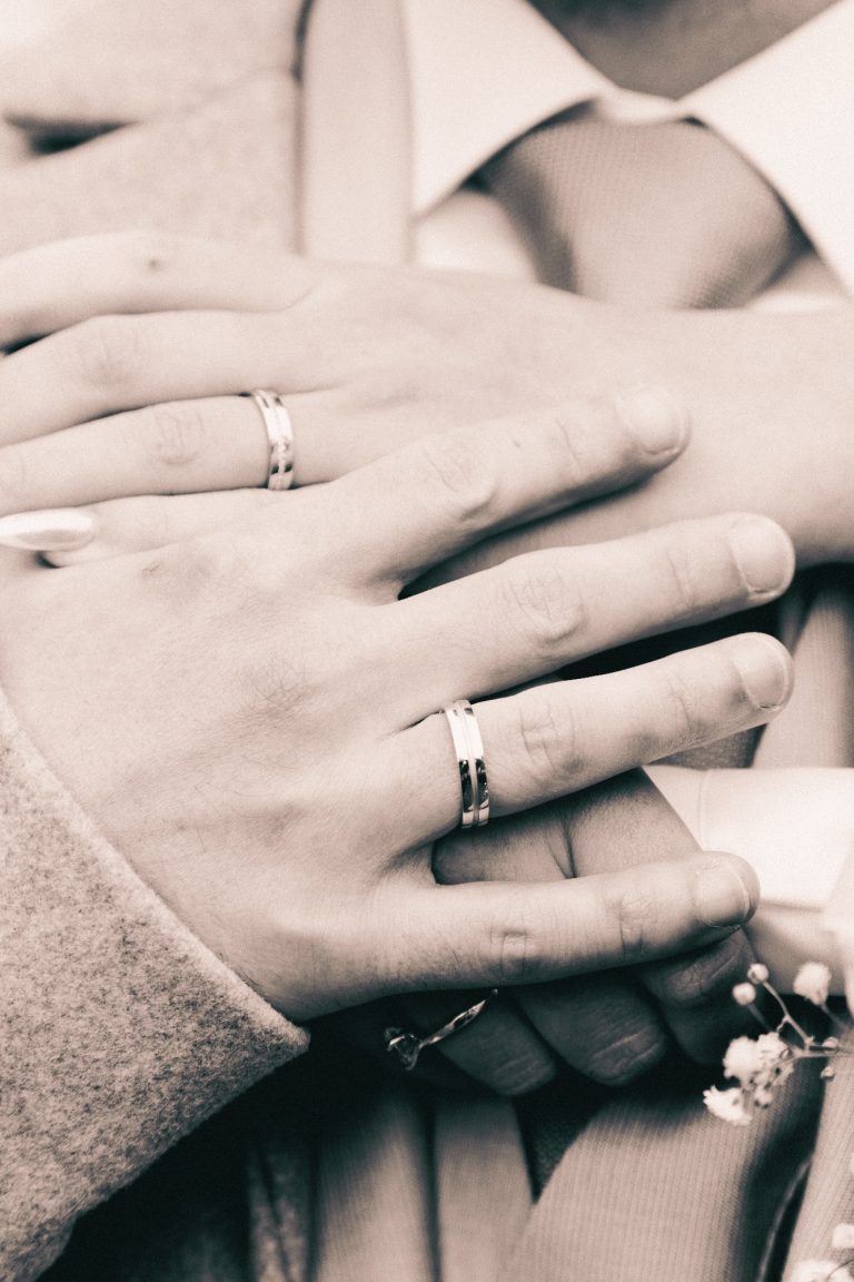 Hände mit Eheringen, die sich sanft umarmen, in sepia gefärbten Farben.