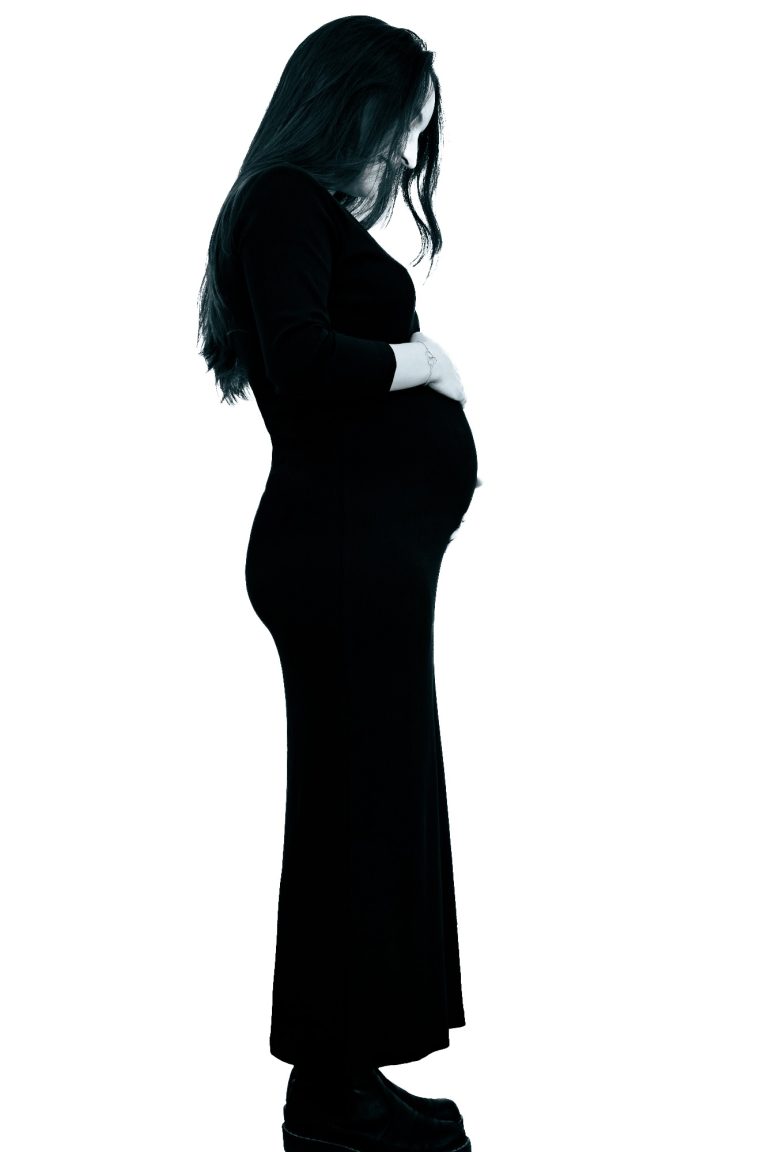 Schwangere Frau in schwarz, seitliche Ansicht, mit Händen auf dem Bauch.
