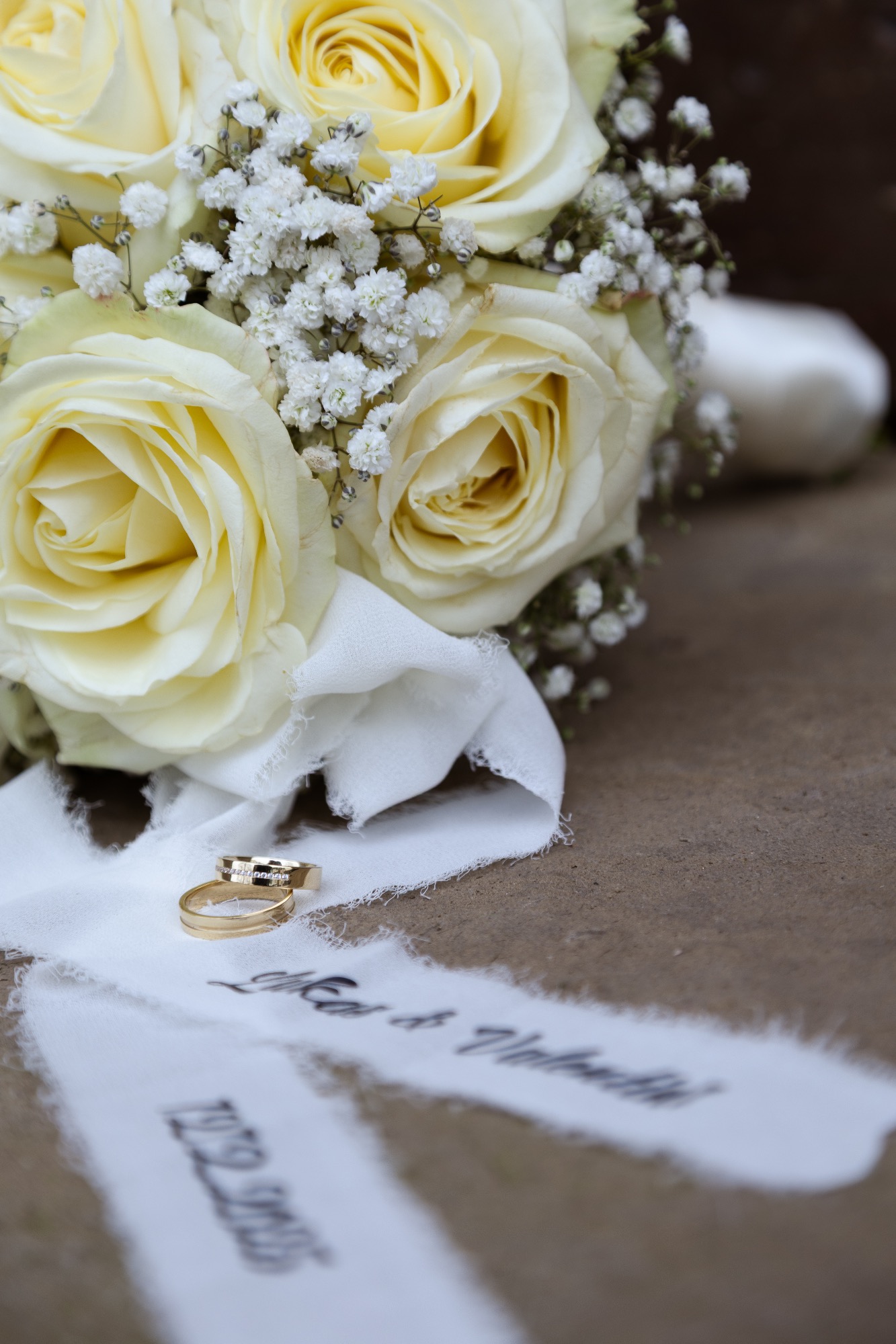 Ein Brautstrauß aus cremefarbenen Rosen mit Gipskraut und zwei Ringen auf weißem Stoff.