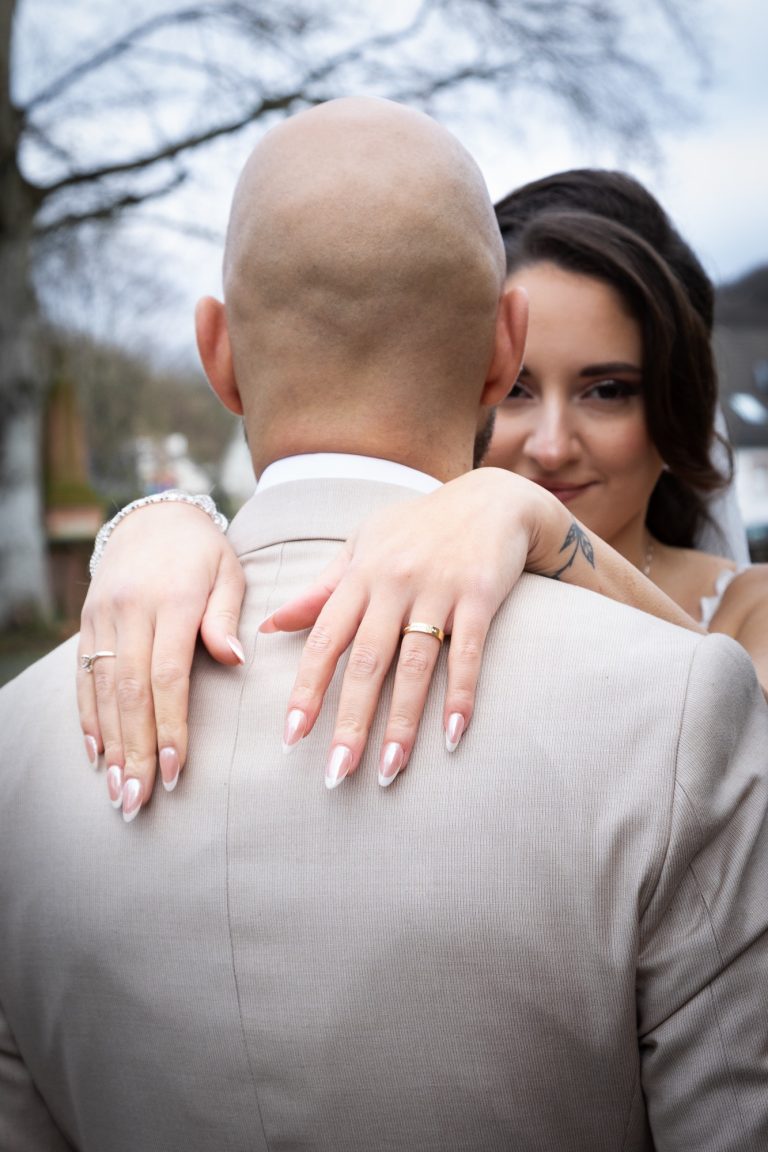 Hochzeitsbraut umarmt ihren Partner, Hände auf dessen Schultern, romantische Atmosphäre.
