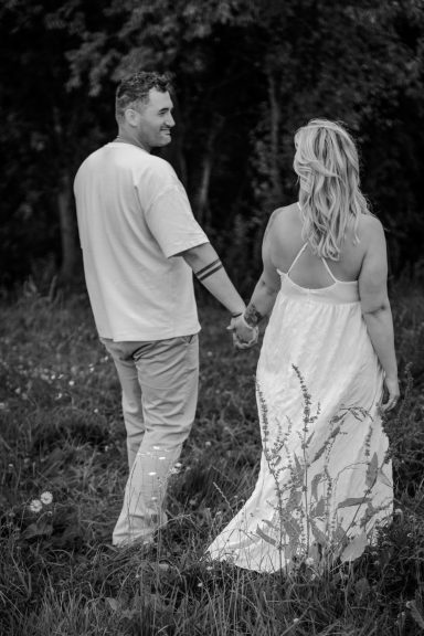 Paar hält Händchen und schaut sich in einer grünen, bewaldeten Umgebung an.