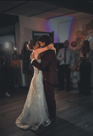 Braut und Bräutigam tanzen eng umschlungen auf der Feier, Gäste beobachten sie.