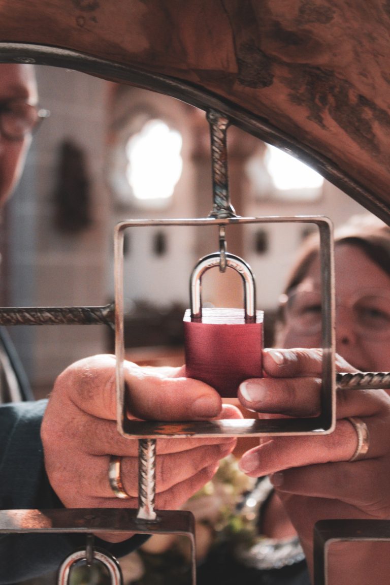 Rote Liebesschloss wird von einer Hand durch eine geometrische Struktur gehalten.
