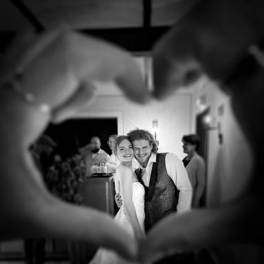 Brautpaar umgeben von Herzen, lächeln vor einer festlichen Kulisse.