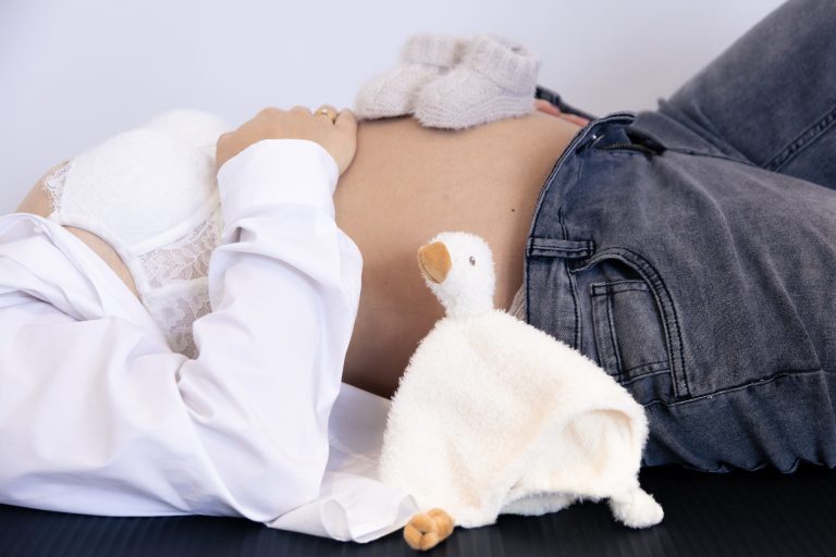 Schwangere Person mit ausgestrecktem Bauch und einem weißen Stofftier daneben.